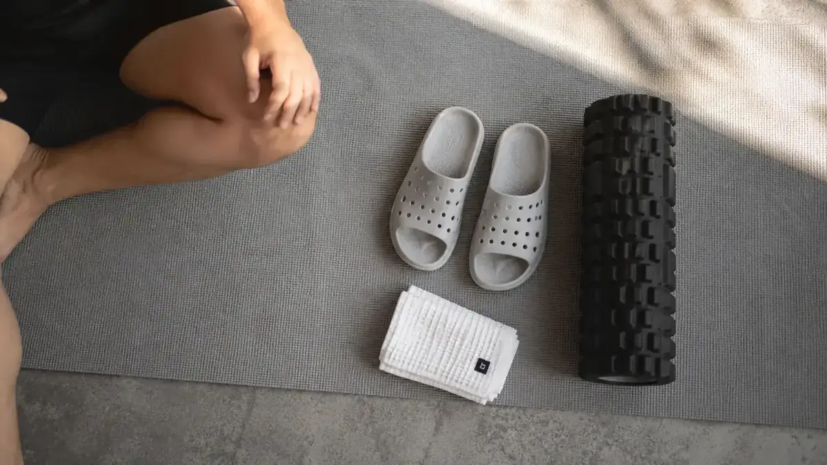 Pair of recovery sandals and a foam roller side by side on a yoga mat, top-down flat lay